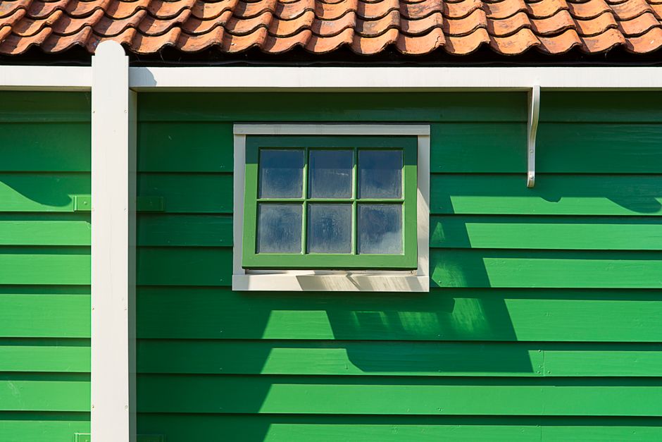 Close-up of a vibrant green wooden house with a small window and terracotta tile roof.